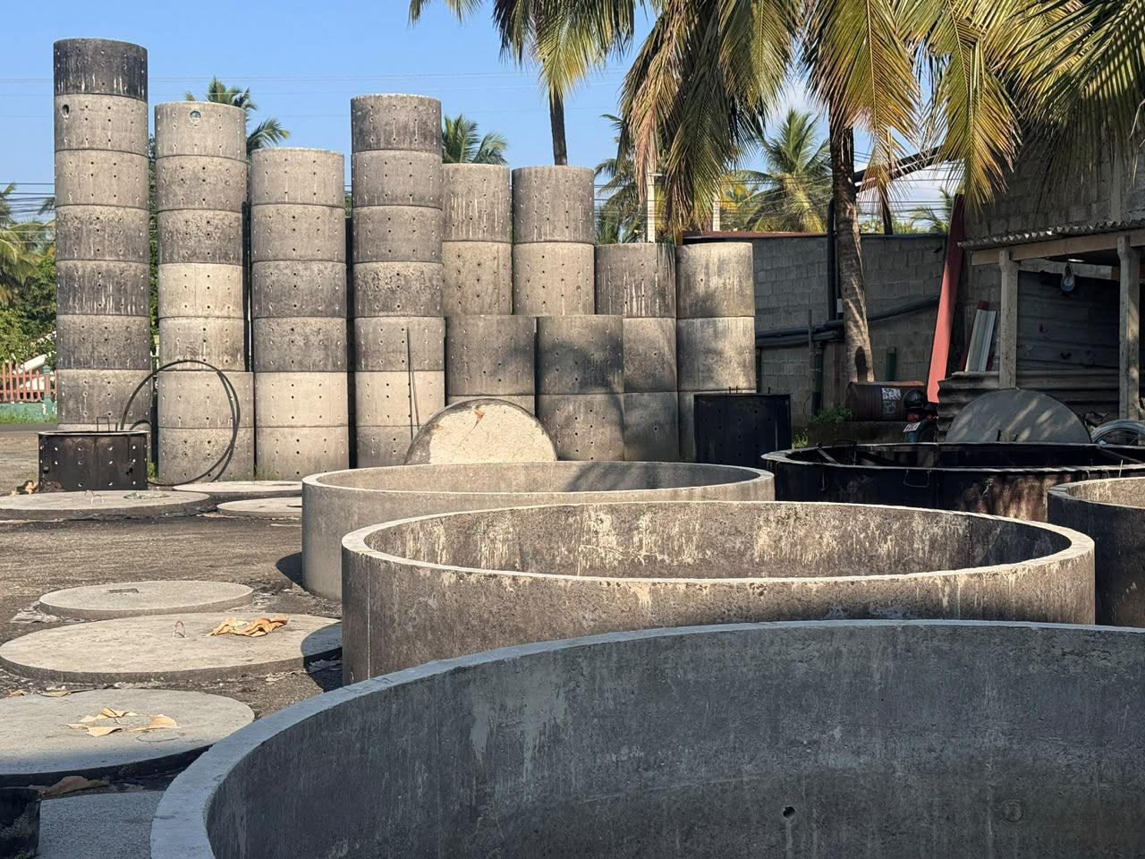 Perforated concrete soakage rings stacked in tall columns in the Ajith Concrete Works yard, with large rings and round cover slabs in front