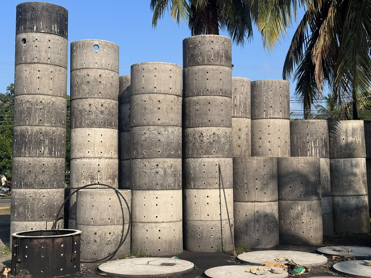 Perforated concrete soakage rings stacked in the yard, with rows of holes through the wall