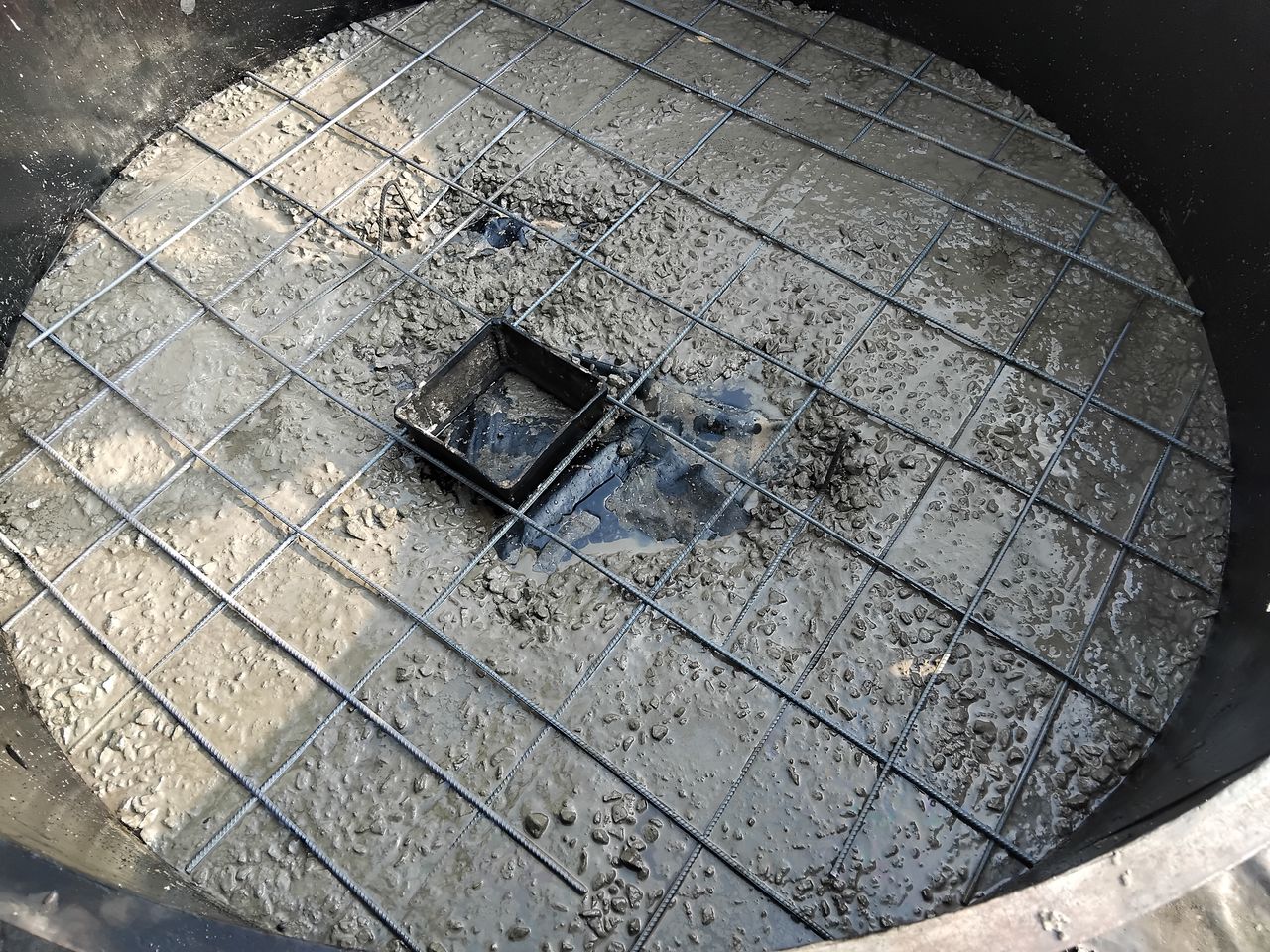 A round cover slab being cast in its mould, with steel mesh in the concrete and a square form for the access opening