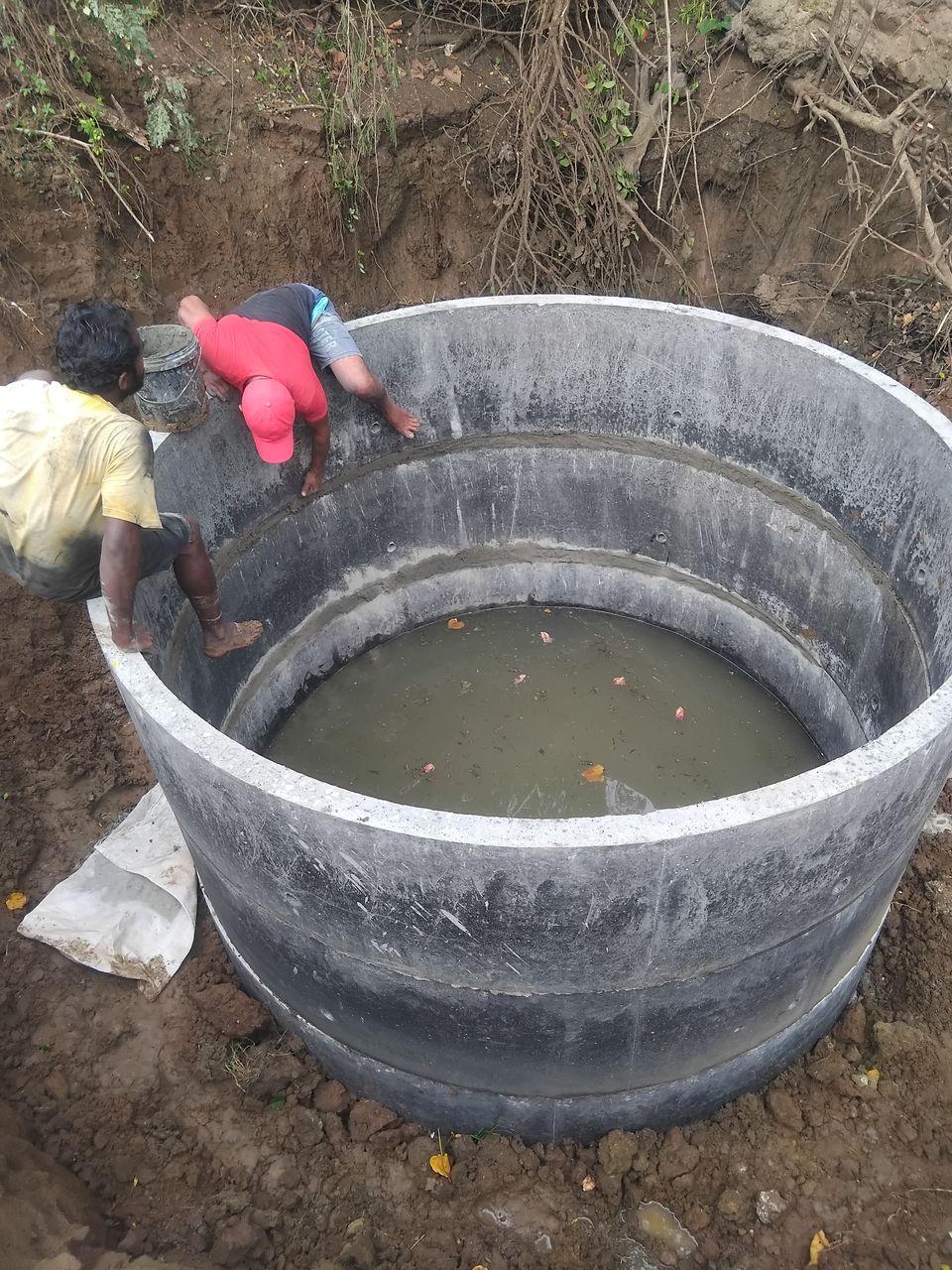 Two workers at the rim of a large chamber built from two concrete rings, water at the bottom