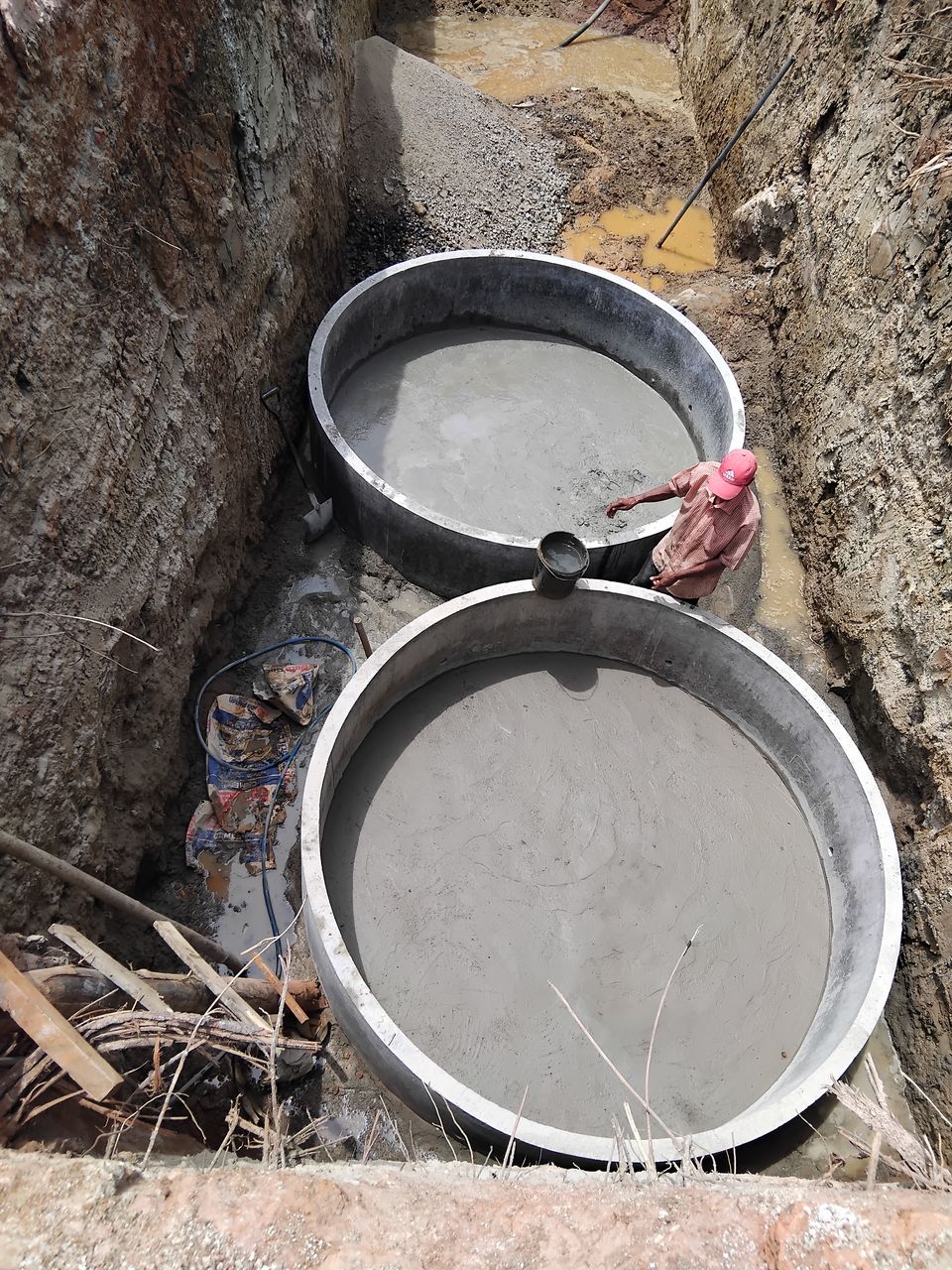 Two large concrete rings set on a fresh concrete base at the bottom of a long, deep excavation
