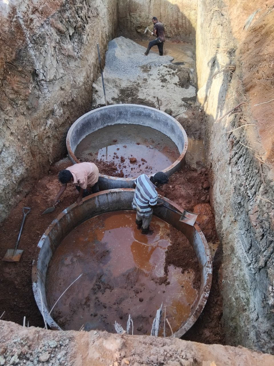 Workers inside two large concrete rings at the bottom of a long excavation