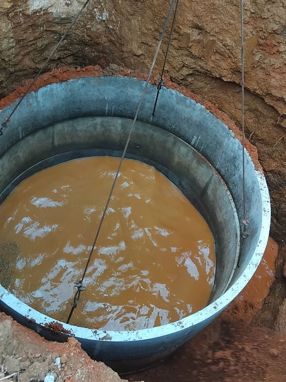 A concrete ring lowered by crane into a well pit full of water
