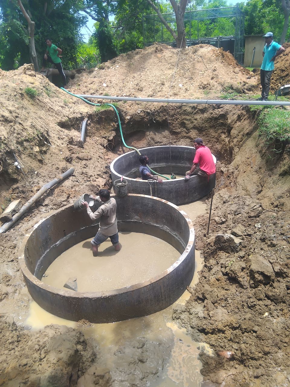 Two large concrete rings set on concrete bases in a wide, wet pit, with workers inside