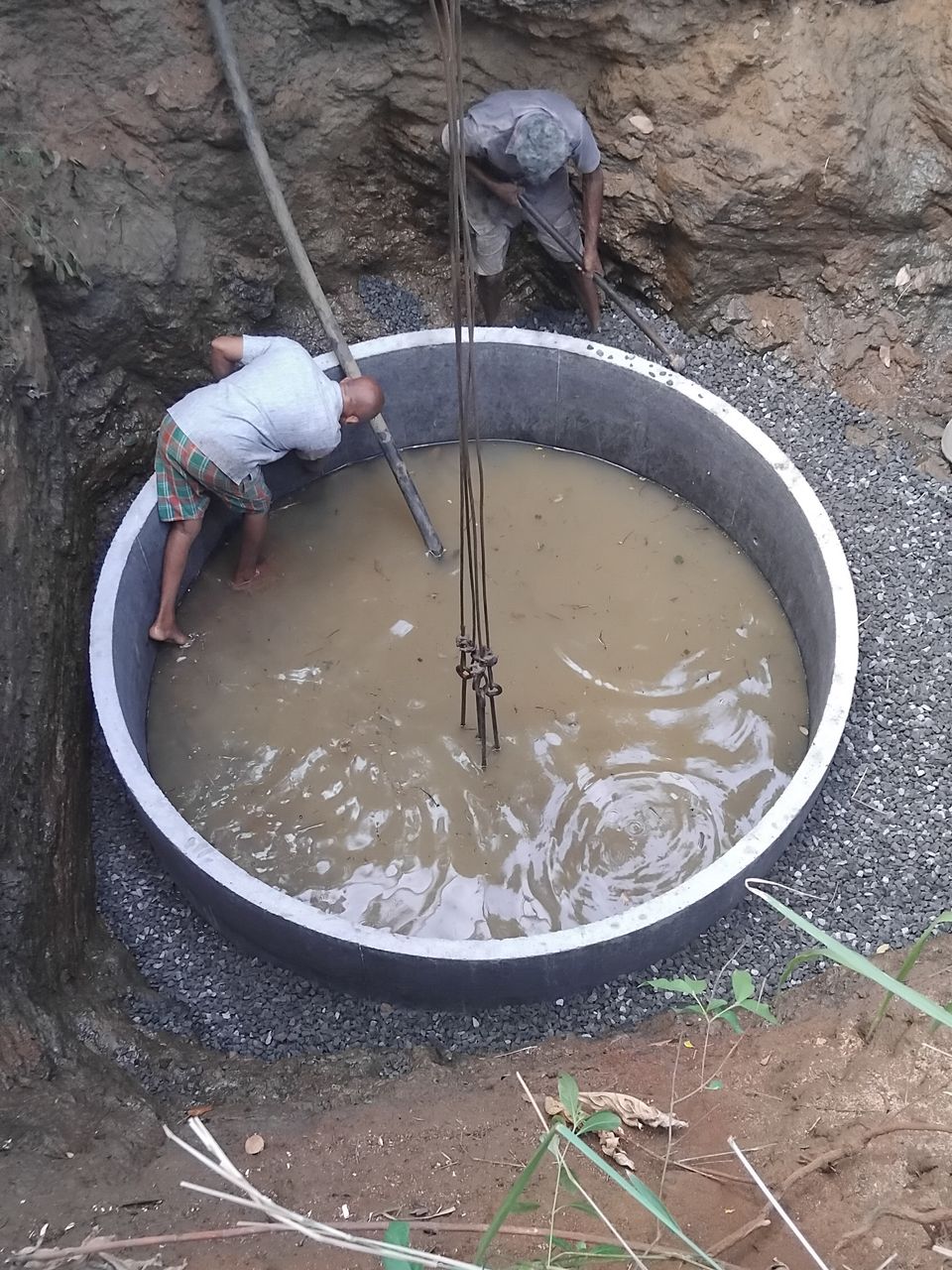 Workers setting the bottom concrete ring of a new well level, the crane chains still attached, with gravel around it