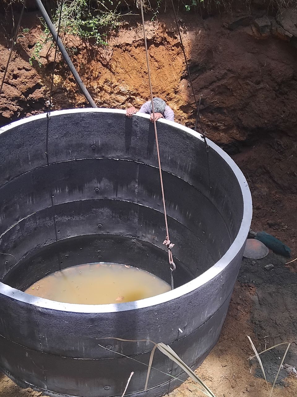 Concrete well rings stacked in a pit with water at the bottom, the crane slings still on the top ring