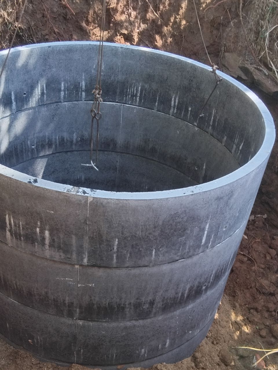 The top concrete rings of a new well at ground level, still on the crane slings